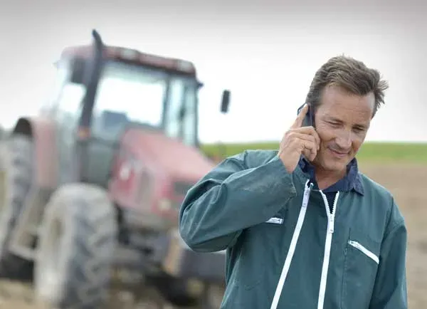 Asesor agrícola hablando por teléfono junto a un tractor